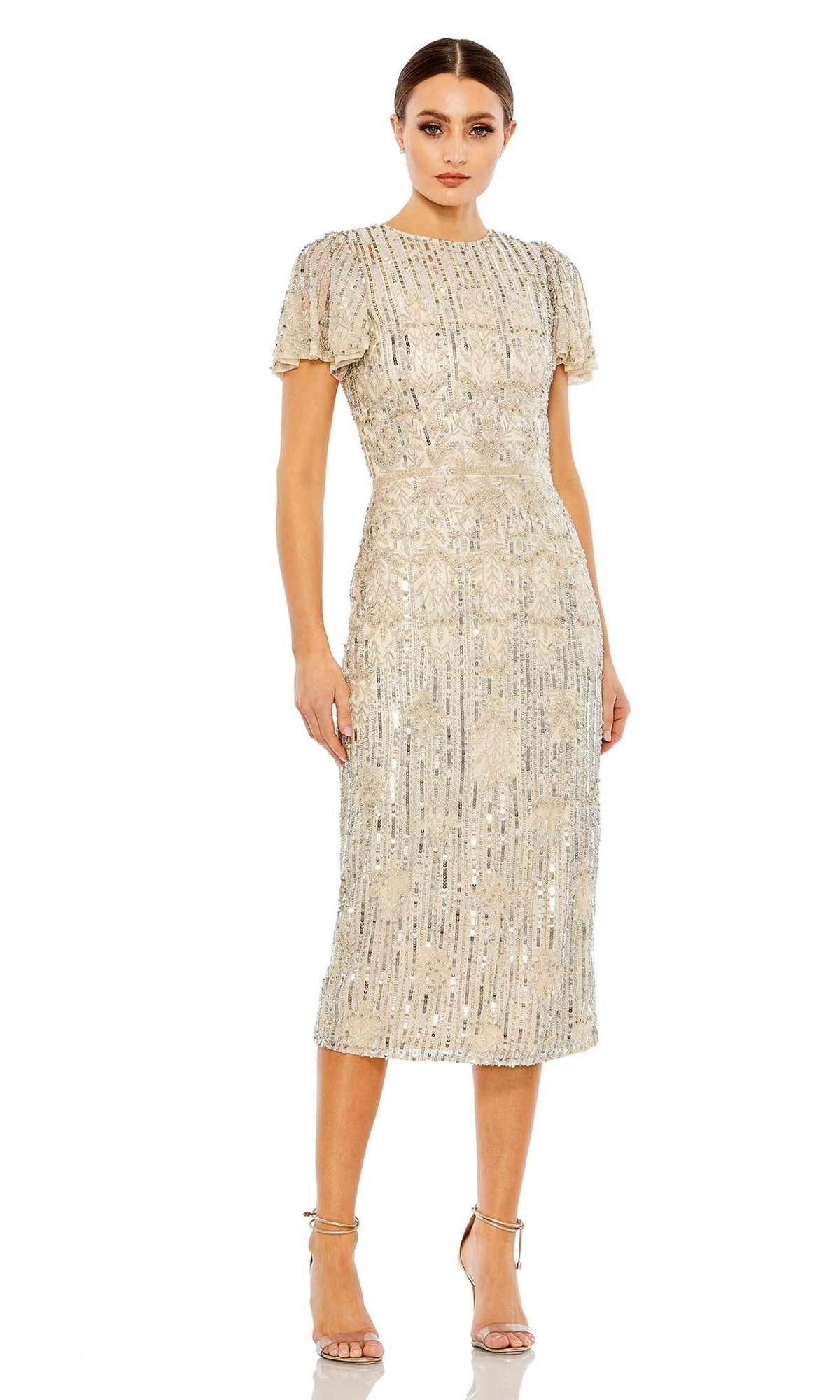 A woman wears the Mac Duggal Short Semi-Formal Dress 5575, a cream midi dress with silver beading and short sleeves, styled with strappy high-heeled sandals.